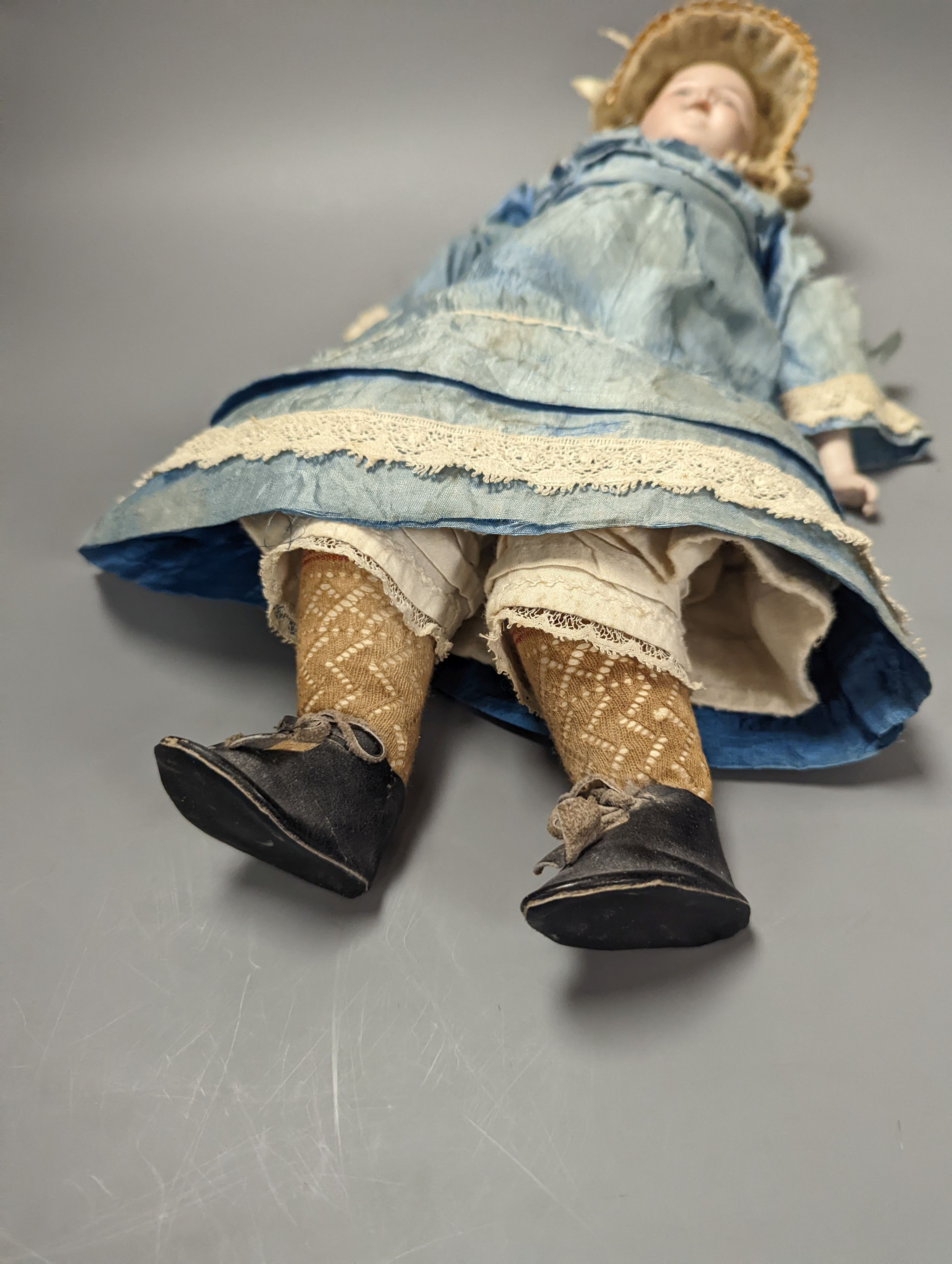 A German bisque headed doll, wearing a blue silk dress and straw bonnet, 42 cms high.